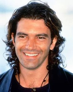 a man with long hair smiling at the camera and wearing a leather jacket over his shoulders