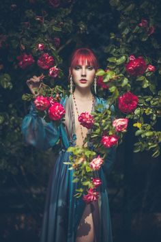 a woman with red hair wearing a blue dress surrounded by roses