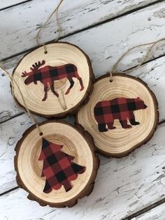 three wooden ornaments with moose designs on them hanging from twine strings against a white wood background