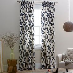 a living room filled with furniture and a large window covered in blue draperies next to a white chair