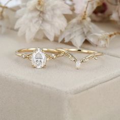 two gold rings with white stones and leaves on the side, sitting next to flowers