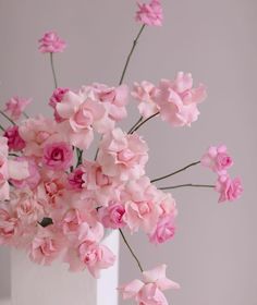 a white vase filled with pink flowers on top of a table