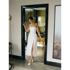 a woman standing in front of a doorway wearing a white dress with high slits