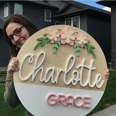 a woman holding up a sign that says charlotte grace in front of her house with flowers on it