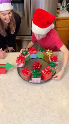 two girls in santa hats are decorating presents on a table with an arrow pointing to them