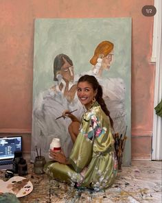 a woman sitting on the floor in front of a painting and holding a coffee cup