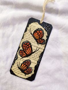 a bookmark with two orange butterflies on it hanging from a string and white background