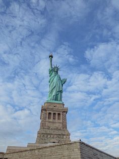 the statue of liberty stands tall in front of a cloudy blue sky