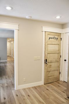 an empty living room with wood floors and white walls, has a door leading to the kitchen