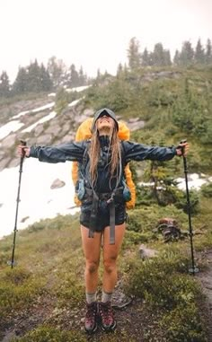 a woman standing on top of a grass covered hillside with ski poles in her hands