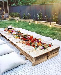 a long table is set up outside with food on it and lit candles in the background