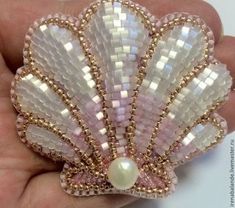 a hand holding a pink and white brooch with pearls on it's side