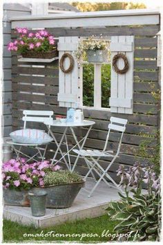 an outdoor table and chairs with potted flowers in front of the window, next to a wooden fence