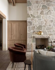 a living room with stone wall and fireplace in it, surrounded by chairs and tables