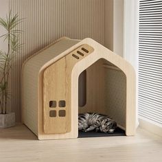 a small wooden house with a cat sleeping in it's bed next to a potted plant