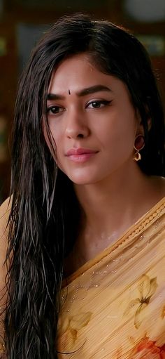 a woman with long black hair wearing a yellow sari and gold earrings