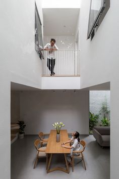 a person sitting at a table in a room with high ceilings and stairs to the second floor