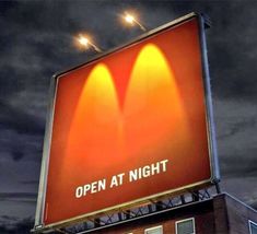 an open at night sign on the side of a building in front of dark clouds