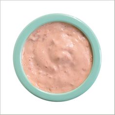 a green bowl filled with pink sauce on top of a white table next to a blue plate