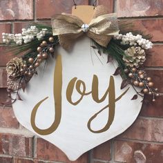 a joy sign hanging on the side of a brick wall with pine cones and berries