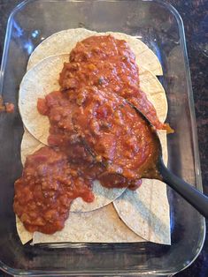 two tortillas covered in sauce on top of a glass dish with a spoon