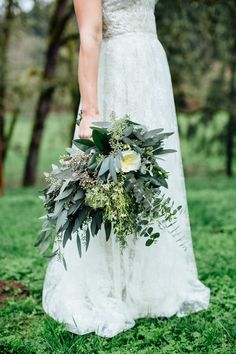 a woman in a white dress holding a bridal bouquet with greenery and flowers