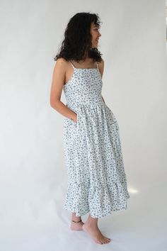 a woman standing in front of a white background wearing a dress with blue flowers on it