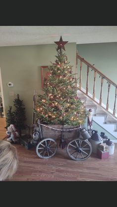 a small christmas tree in a wagon with lights on it's sides and presents under the stairs