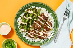 a green plate topped with meat and asparagus next to a bowl of sauce