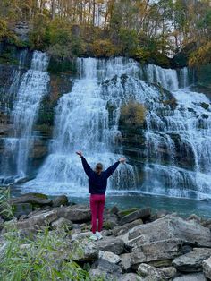 a woman standing in front of a waterfall with her arms wide open and hands up