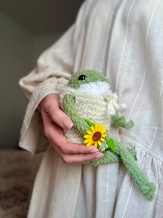 a person holding a small stuffed animal with a flower in it's hand and wearing a white dress