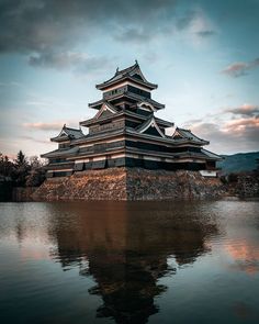 a tall building sitting on top of a lake next to a mountain under a cloudy sky