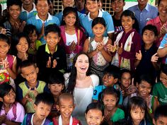 a woman standing in front of a large group of children with their hands up and smiling