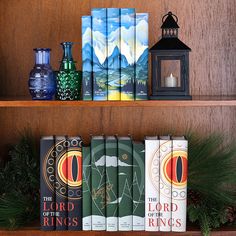 several books on a shelf next to a lantern and some pine branches in front of them