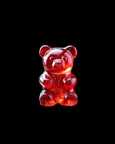 a red glass teddy bear sitting on top of a black surface with its eyes closed