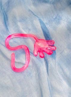 a pink plastic toy monkey laying on top of a blue cloth covered bed sheet with it's tail curled up