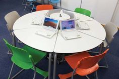 two laptops sitting on top of a round table in an office setting with chairs around it