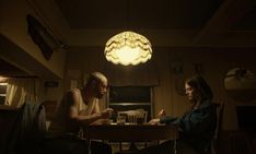 a man and woman sitting at a table in a dark room with a light hanging from the ceiling