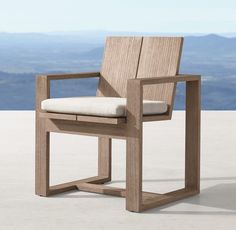 a wooden chair sitting on top of a cement floor next to a mountain range in the distance