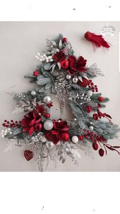 a christmas wreath hanging on the wall with red and white decorations, holly berries and mist cones