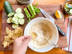 a person is dipping some kind of dip in a bowl with cucumbers and celery