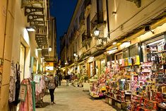 people are walking down an alley way in the city at night with shops on both sides