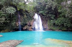 a large waterfall in the middle of a body of water with wooden rafters floating on it