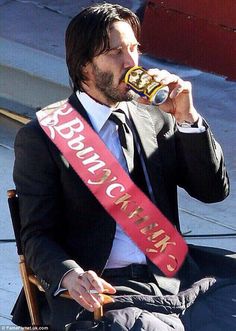 a man in a suit and tie drinking from a can while sitting on a chair