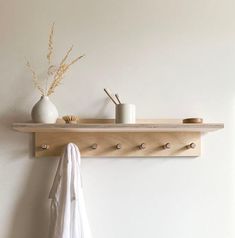 a white vase sitting on top of a wooden shelf next to a wall mounted coat rack