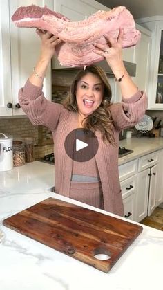 a woman standing in a kitchen holding up a large piece of meat over her head