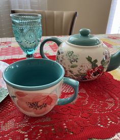 two teapots and a cup on a red tablecloth with lace doily