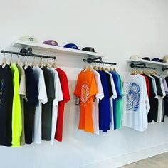 there are many shirts hanging up on the wall in this room with hats and baseball caps