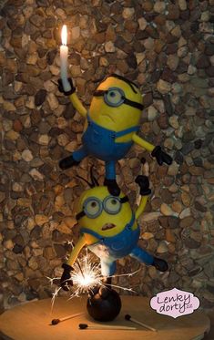 two minion figures holding sparklers on top of a wooden table next to a stone wall