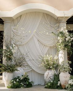 an outdoor wedding ceremony with white flowers and greenery on the stage, surrounded by large vases